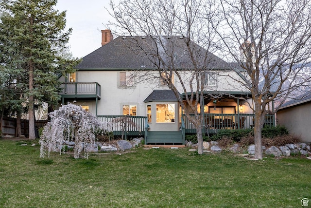 rear view of property with roof with shingles, a deck, a yard, stucco siding, and a chimney