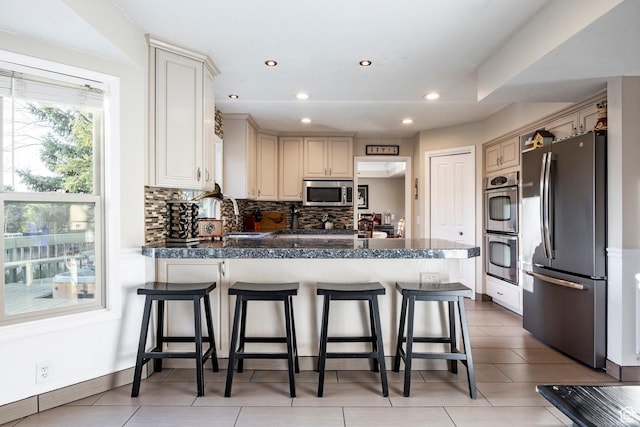 kitchen with a peninsula, recessed lighting, backsplash, a kitchen bar, and appliances with stainless steel finishes