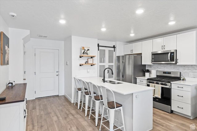 kitchen with open shelves, a sink, a breakfast bar area, stainless steel appliances, and visible vents