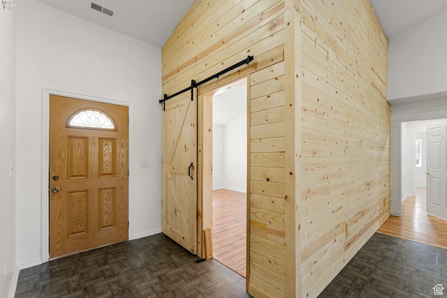 entrance foyer featuring a barn door, wooden walls, visible vents, baseboards, and high vaulted ceiling