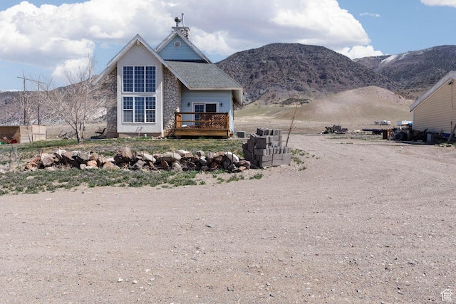 exterior space with a shingled roof, dirt driveway, and a deck with mountain view