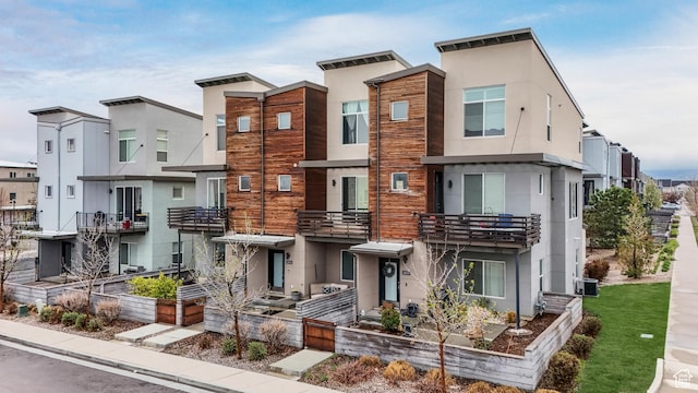 townhome / multi-family property featuring a balcony, central AC, a residential view, and stucco siding