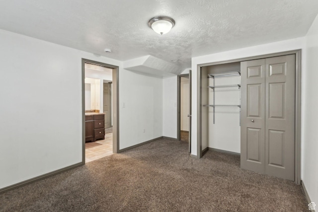 unfurnished bedroom with ensuite bathroom, a textured ceiling, a closet, light carpet, and baseboards