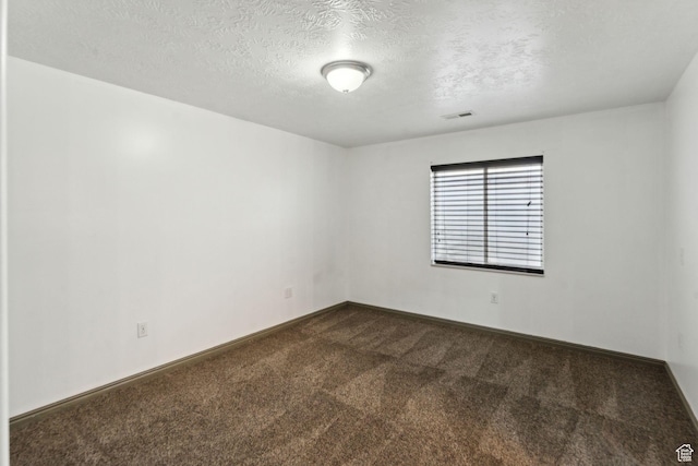 spare room featuring a textured ceiling, dark colored carpet, visible vents, and baseboards