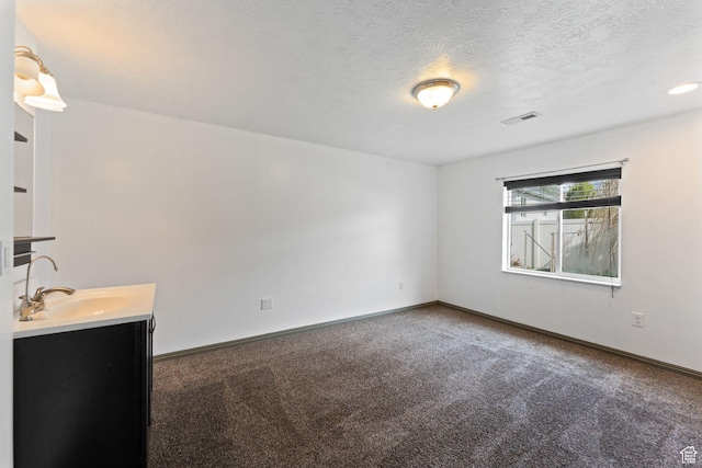carpeted empty room featuring baseboards, visible vents, a sink, and a textured ceiling