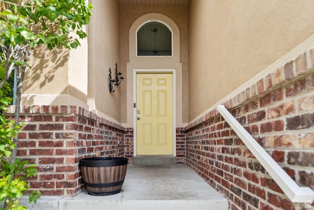 view of exterior entry featuring brick siding and stucco siding