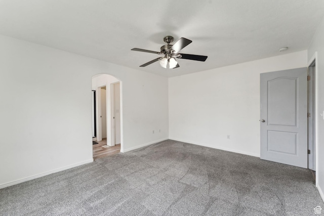 carpeted empty room featuring arched walkways, a ceiling fan, and baseboards