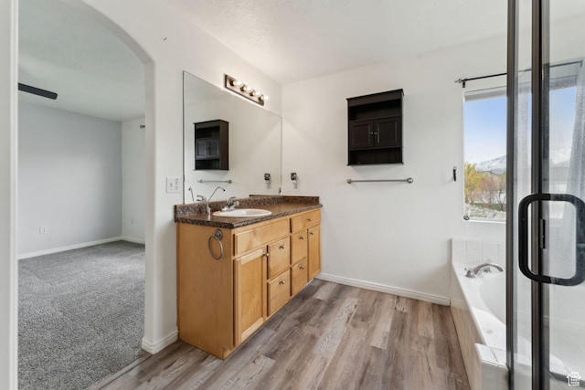 bathroom featuring baseboards, a bath, wood finished floors, and vanity