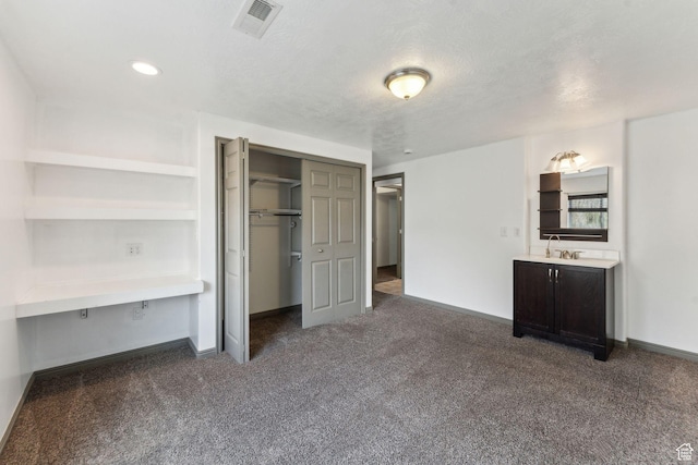 unfurnished bedroom with dark colored carpet, a closet, baseboards, and a sink