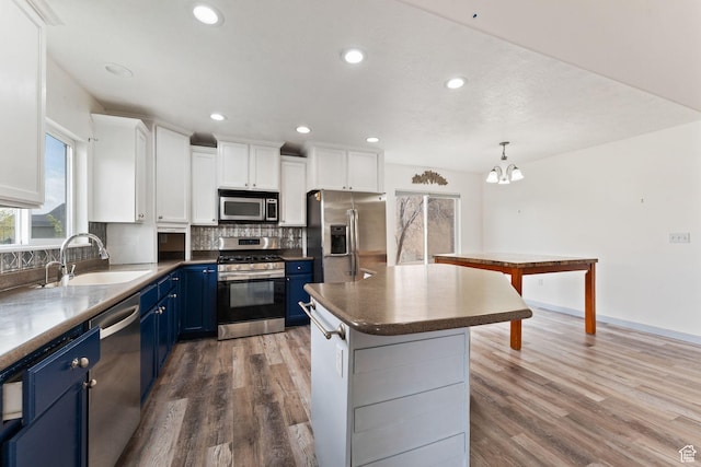 kitchen featuring white cabinets, stainless steel appliances, a sink, tasteful backsplash, and blue cabinetry