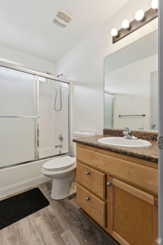 bathroom featuring bath / shower combo with glass door, toilet, visible vents, wood finished floors, and vanity