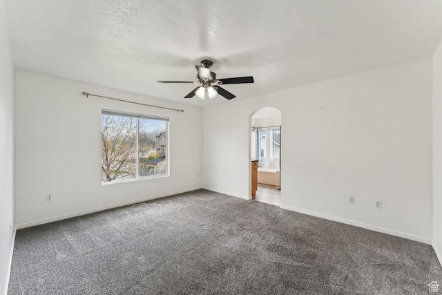 carpeted empty room featuring baseboards, arched walkways, a textured ceiling, and ceiling fan