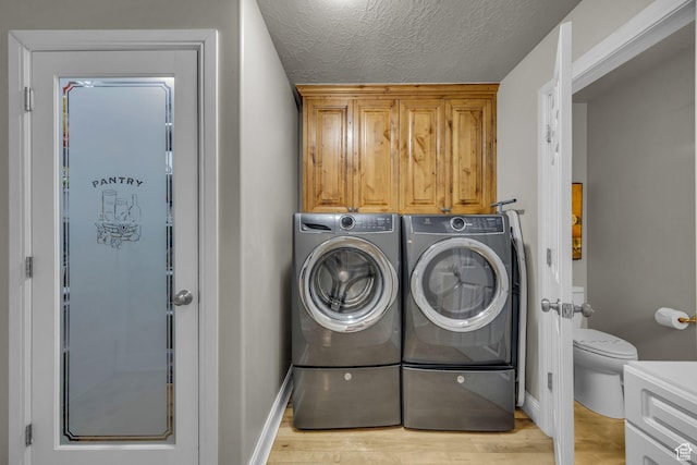 clothes washing area featuring washer and clothes dryer, a textured ceiling, light wood-style floors, cabinet space, and baseboards