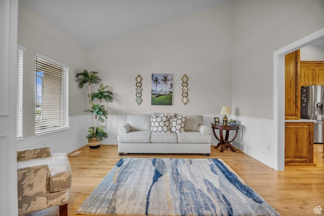 living room with vaulted ceiling, a decorative wall, light wood finished floors, and a wainscoted wall