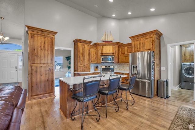 kitchen featuring light countertops, light wood-style floors, appliances with stainless steel finishes, high vaulted ceiling, and washer / clothes dryer