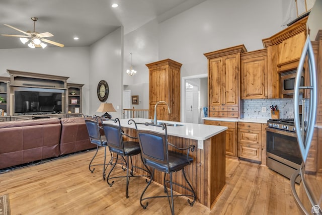 kitchen with high vaulted ceiling, a sink, a breakfast bar area, ceiling fan, and appliances with stainless steel finishes