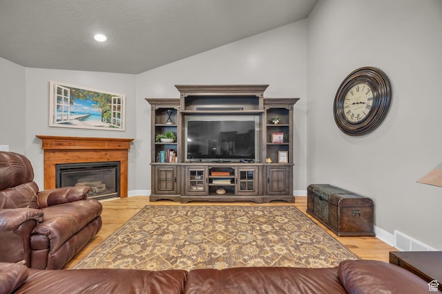 living area featuring vaulted ceiling, visible vents, wood finished floors, baseboards, and a glass covered fireplace