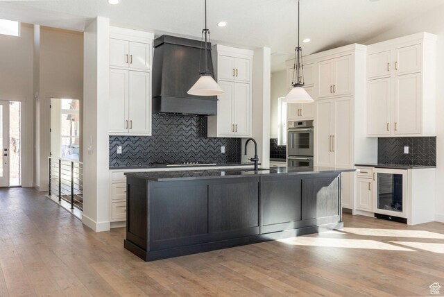 kitchen featuring premium range hood, double oven, beverage cooler, and dark countertops
