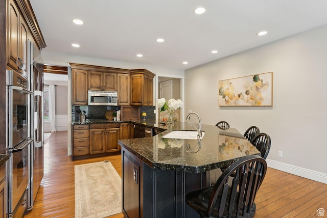 6391 S Shenandoah Park Ave E, Salt Lake City, UT 84121 - kitchen featuring stainless steel appliances, a sink, light wood-type flooring, decorative backsplash, and a kitchen bar