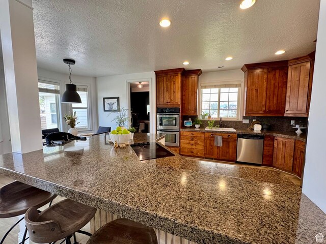 1844 W Heritage Ranch Dr N, Farr West, UT 84404 - kitchen featuring stainless steel appliances, a kitchen breakfast bar, a textured ceiling, a sink, and brown cabinetry