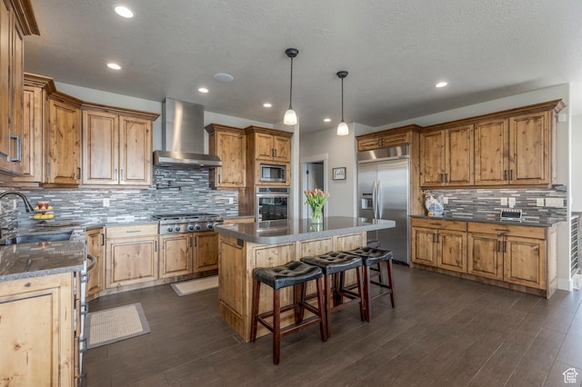 kitchen with built in appliances, wall chimney range hood, a sink, decorative backsplash, and a center island