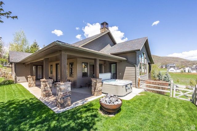 rear view of property featuring a patio, a shingled roof, a hot tub, a chimney, and a mountain view