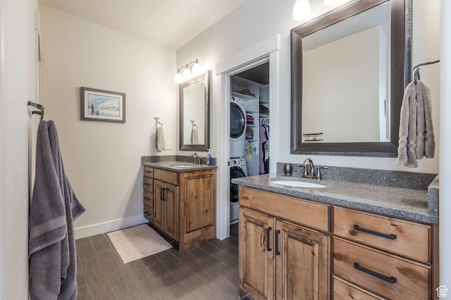 bathroom with stacked washer / dryer, wood finished floors, two vanities, baseboards, and a walk in closet