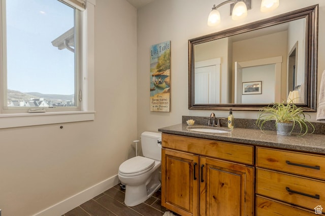 half bath with healthy amount of natural light, baseboards, wood finished floors, and toilet