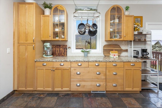 kitchen featuring decorative backsplash, stone tile flooring, and glass insert cabinets