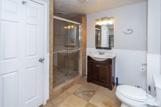 bathroom with a textured ceiling, toilet, wainscoting, a shower stall, and vanity