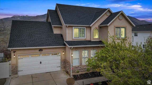 view of front facade with stucco siding, driveway, stone siding, roof with shingles, and a mountain view