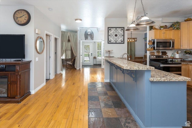 kitchen featuring light wood-style floors, pendant lighting, backsplash, appliances with stainless steel finishes, and light stone countertops