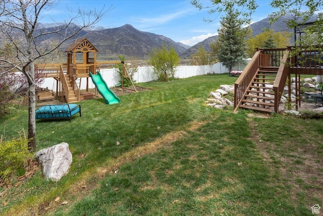 view of play area with fence, a deck with mountain view, a yard, and stairway