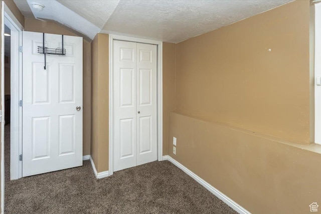 unfurnished bedroom with a closet, dark colored carpet, a textured ceiling, and baseboards