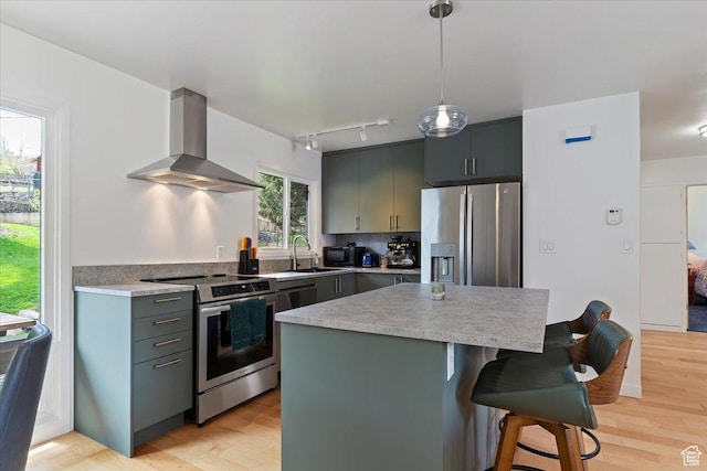 3315 Meadow Dr, Ogden, UT 84403 - kitchen featuring wall chimney range hood, a sink, a kitchen bar, rail lighting, and appliances with stainless steel finishes