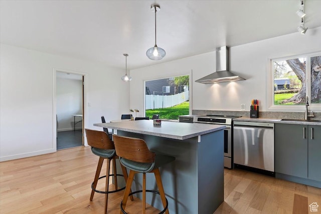 3315 Meadow Dr, Ogden, UT 84403 - kitchen with light wood finished floors, stainless steel appliances, a sink, wall chimney range hood, and a breakfast bar