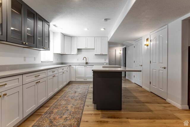 637 S Pine Meadow Ln, Tooele, UT 84074 - kitchen featuring light wood-style flooring, a textured ceiling, a center island, and glass insert cabinets