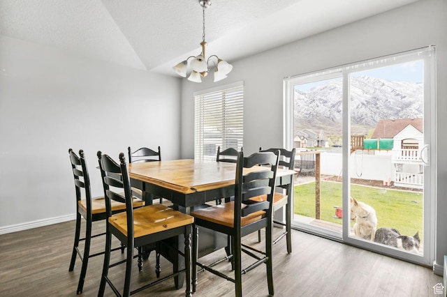 dining room with a mountain view, baseboards, a chandelier, lofted ceiling, and wood finished floors