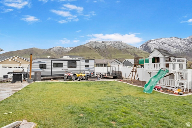back of house featuring a yard, a playground, fence, and a mountain view