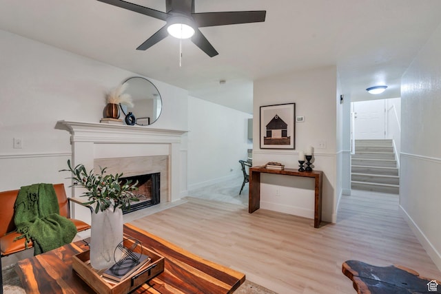 living area with light wood-style floors, stairs, a ceiling fan, and baseboards