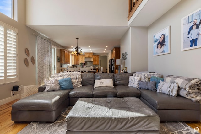 living area with a towering ceiling, baseboards, recessed lighting, a chandelier, and wood finished floors