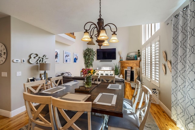 dining room with a fireplace, baseboards, light wood-style floors, and an inviting chandelier