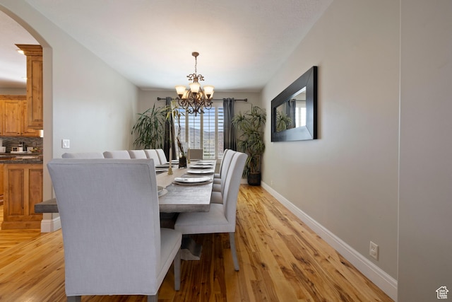 dining area featuring light wood-style flooring, baseboards, arched walkways, and a chandelier