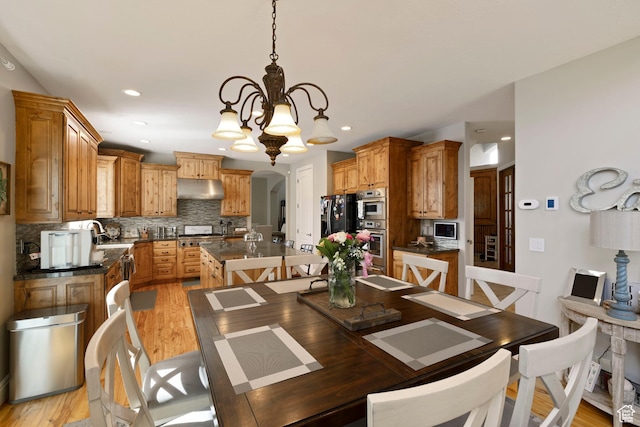 dining room with a chandelier, arched walkways, light wood finished floors, and recessed lighting
