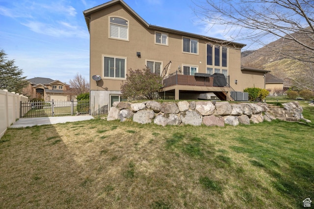 rear view of property featuring a wooden deck, a lawn, stucco siding, and fence