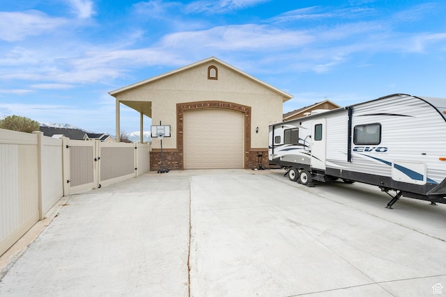 view of side of property featuring stucco siding, a gate, fence, concrete driveway, and an attached garage