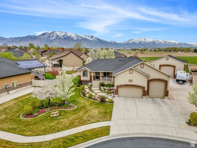 ranch-style home featuring concrete driveway, covered porch, a front yard, a mountain view, and an attached garage