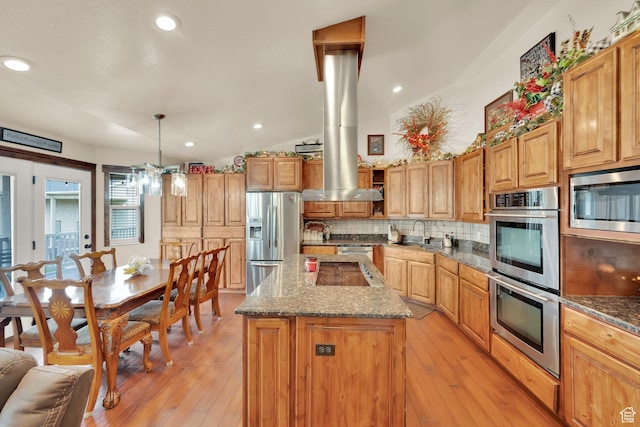 kitchen with a sink, appliances with stainless steel finishes, light wood-style floors, a kitchen island, and backsplash