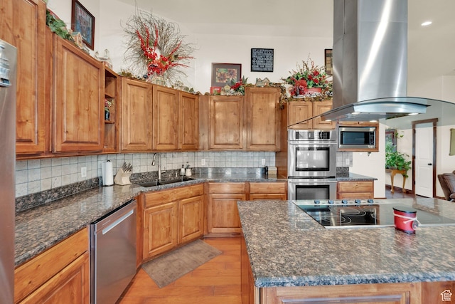 kitchen with a sink, stainless steel appliances, island exhaust hood, brown cabinetry, and backsplash