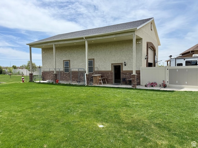 back of house with stucco siding, fence, a lawn, and a patio